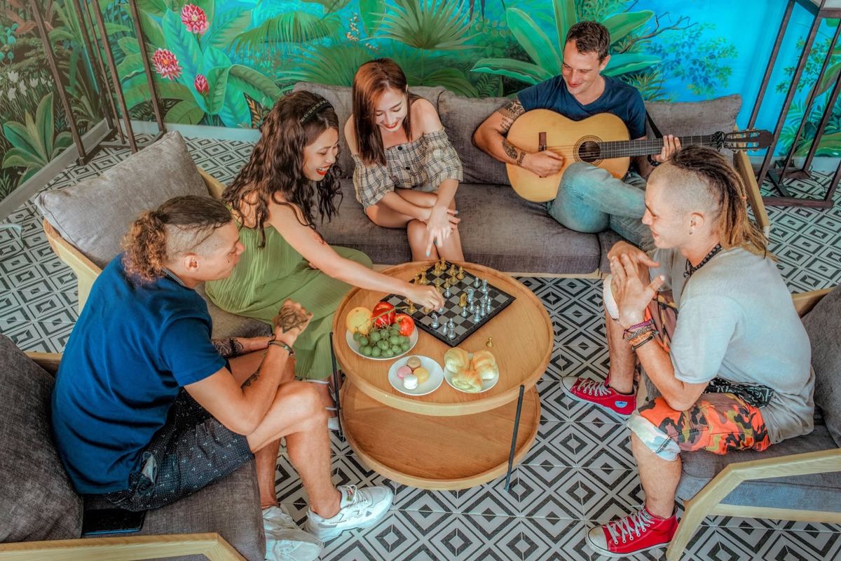 Friends playing chess and guitar on sofas in a lounge with a jungle mural